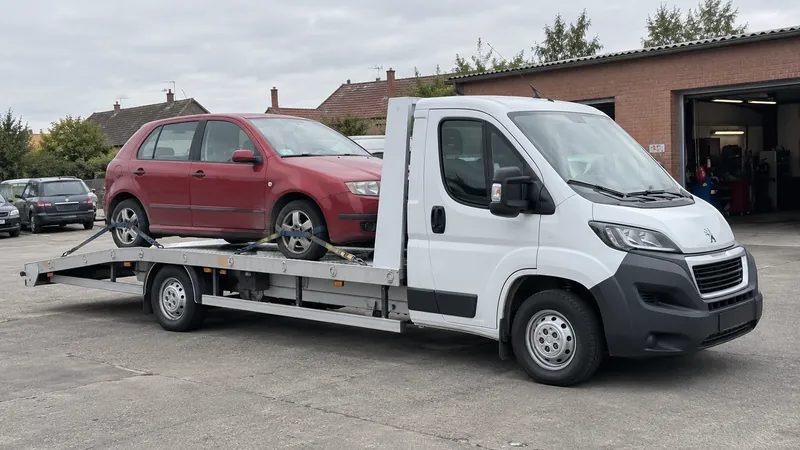 Lehký bílý odtahový vůz s upevněným automobilem Škoda