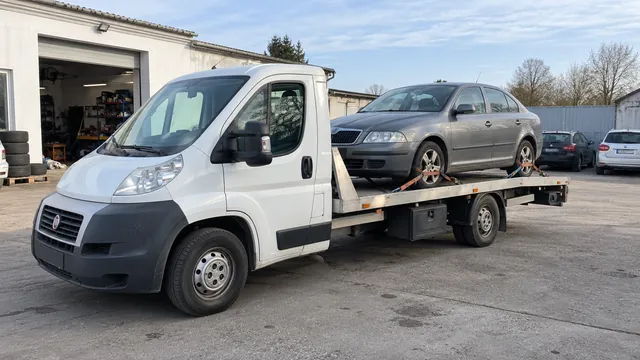 Bílý odtahový vůz s upevněným vozidlem Škoda na hliníkové plošině