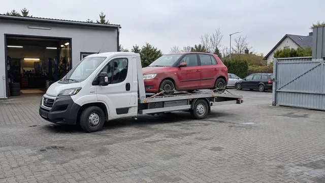 Bílý odtahový vůz s upevněným vozidlem Škoda na hliníkové plošině