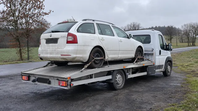 Bílý odtahový vůz s upevněným vozidlem Škoda na hliníkové plošině