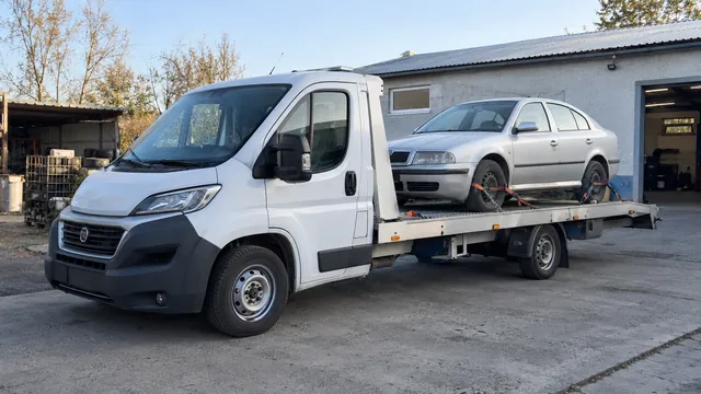 Bílý odtahový vůz s upevněným vozidlem Škoda na hliníkové plošině